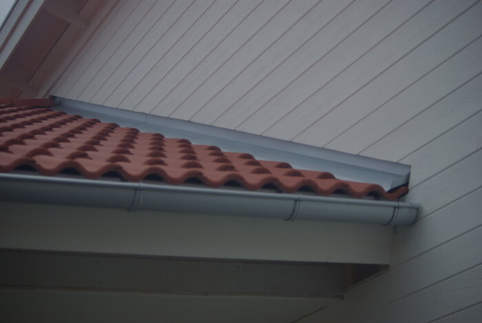 Punainen tiilikatto ja valkoinen seinä, jossa on asennettu sadevesikouru.