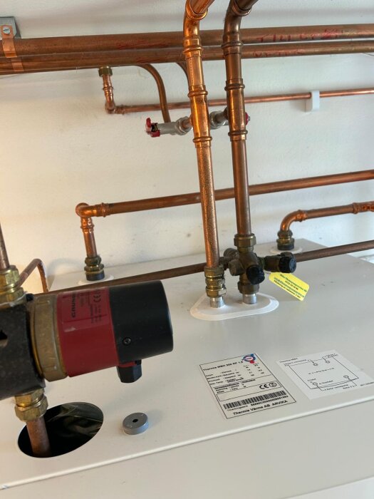 Värmepump med kopparledningar och säkerhetsventil på vänstra maskinen, etikett med Thermia och diagram synliga.