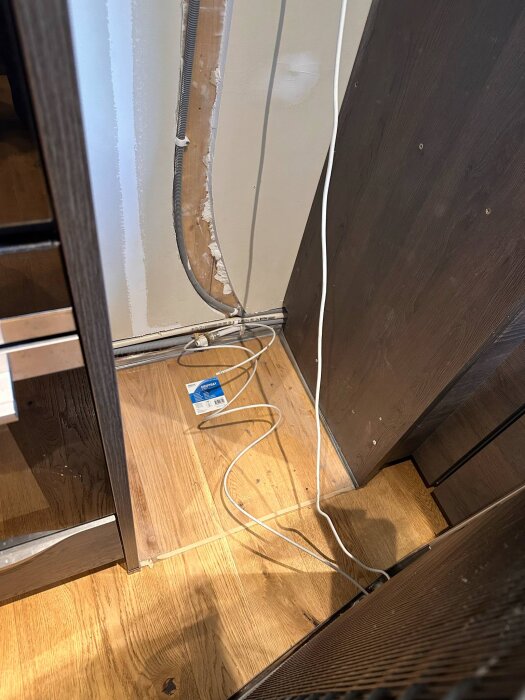 Vattenanslutning med slangar bakom köksskåp, visar området där en översvämning har inträffat.