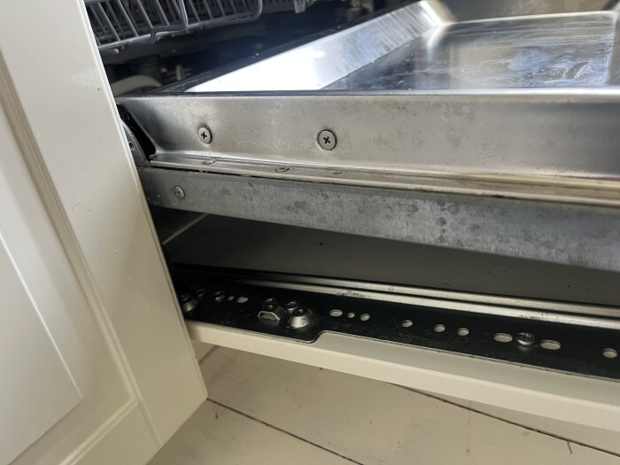 Närbild på kökslucka monterad på diskmaskinslucka, visar skruvar och metalldelar som håller dem samman.