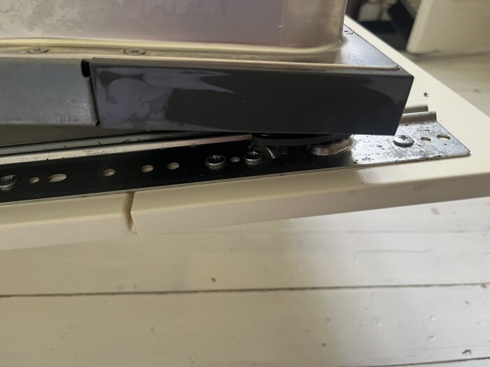 Närbild på gångjärn och skruvar som fäster köksluckan till en integrerad diskmaskin.