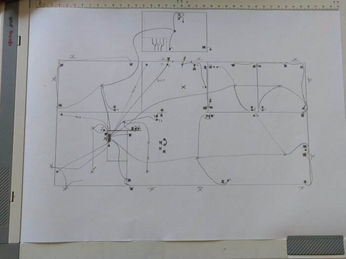 Handritad elektrisk skiss med kablar och komponenter markerade på papper, placerad på ett ritbord med linjaler.