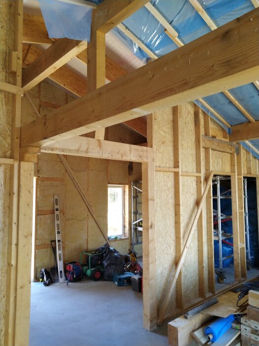 Träram av ett hus under konstruktion, med verktyg och byggmaterial staplade på golvet.