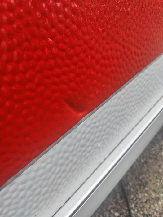 Närbild på röd och vit husvagnsfasad med en liten bula orsakad av en fallande soptunna.