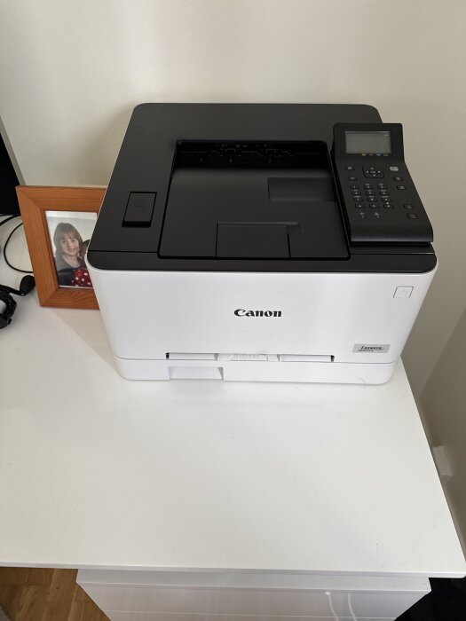 Canon-skrivare på ett skrivbord, bredvid ett inramat foto.