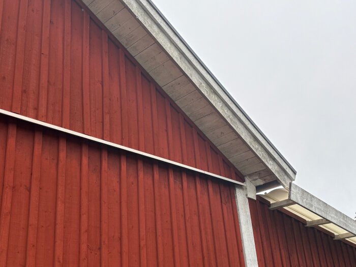 Rött hus med vita vindskivor och takfot, sedd i vinkel. Fokuserar på fasaden och takstrukturen.