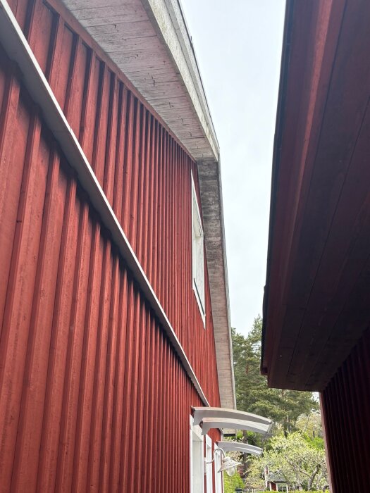 Röd trävägg av 1,5-plansvilla med sadeltak, takutsprång och en lampa över ett fönster. Ljus grå himmel syns ovan.