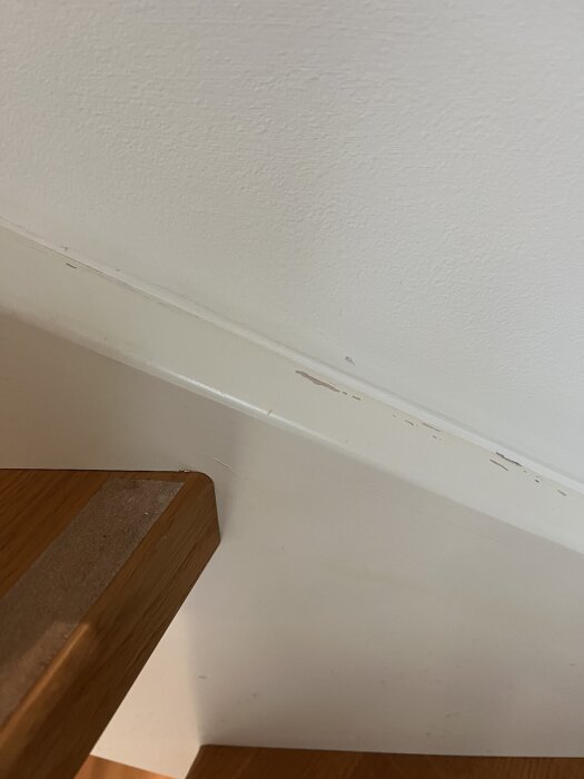 Skador på vitmålat träräcke i trappa, med avskavd yta.
