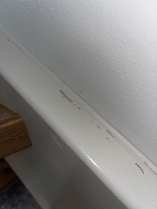 Små skador på vit trappa där färgen har skavts av, visar en sliten yta och träet under.