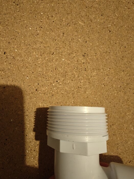 Plastkoppling med gängad ände mot träyta, använd för rörinstallation.