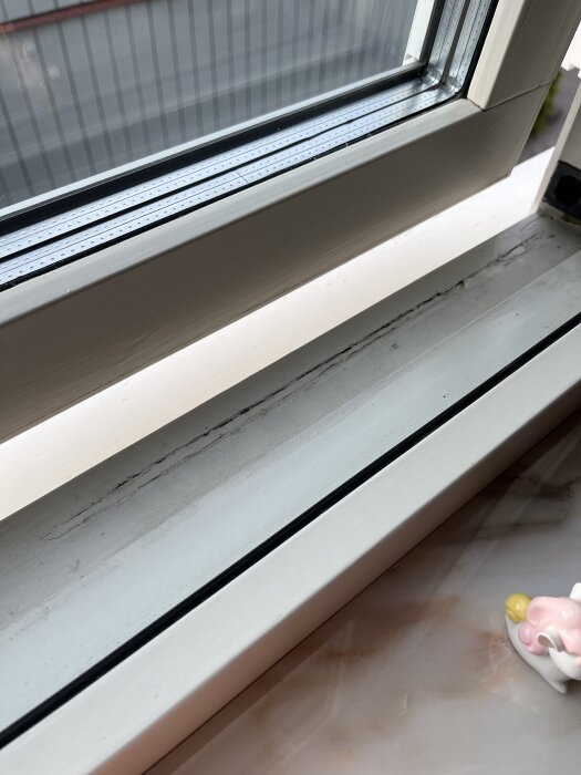 Fönsterbräda med sprickor och skadad färg, frågeställning om reparation med spackel och färg.