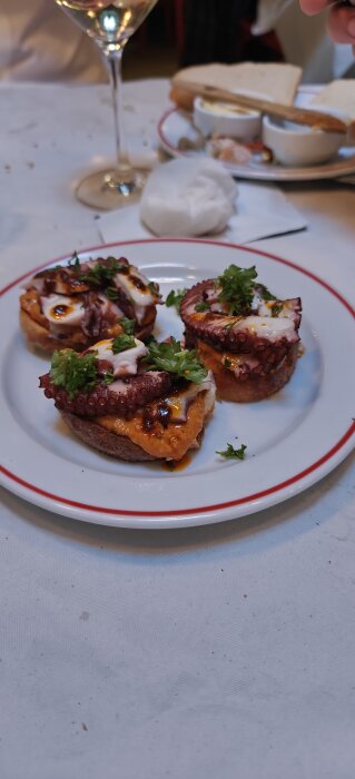 Tre skivor bröd med grillad bläckfisk och persilja på en vit tallrik.
