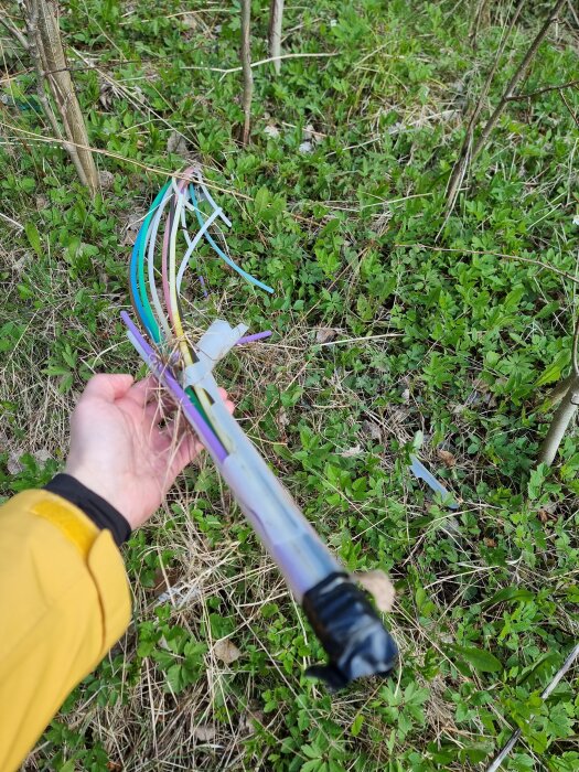 Färgglada, tomma kabelrör i gräset, några tejpade i ändarna, hålls av en person i gul jacka.