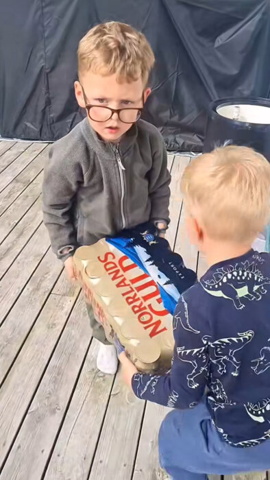 Två barn på en träveranda håller i en förpackning med Norrlands Guld öl.