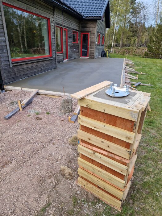 Nygjuten betongplatta framför ett hus med träram för flaggstångsfundament i förgrunden, omgiven av gräs och träd i bakgrunden.
