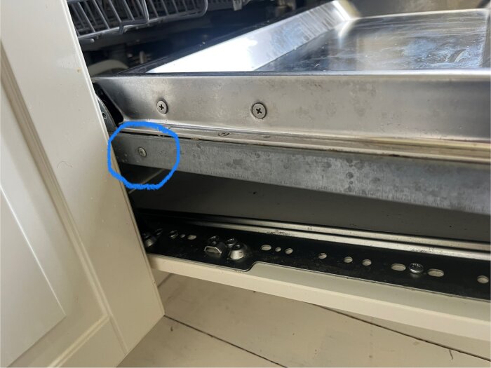 Öppen diskmaskin med fokus på en skruv inuti, markerad med blå cirkel.