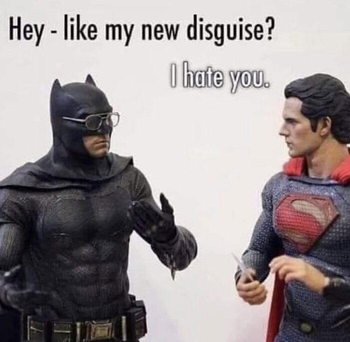 Två actionfigurer, en i svart kostym med glasögon och en i blå kostym med röd symbol, står vända mot varandra. Text: "Hey - like my new disguise?" och "I hate you.