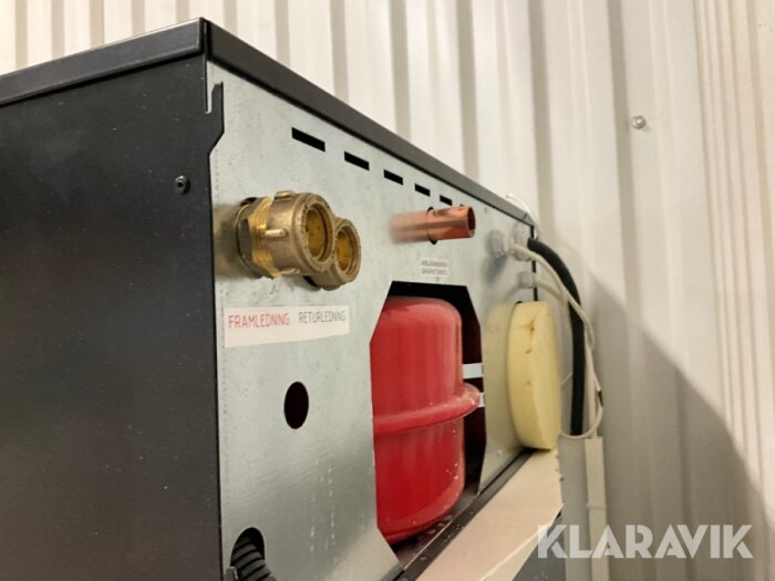 Närbild av elpanna Elomin 3 baksida med två kopplingar märkt "Framledning" och "Returledning", samt en kopparrörskoppling ovanför rostfri skylt.