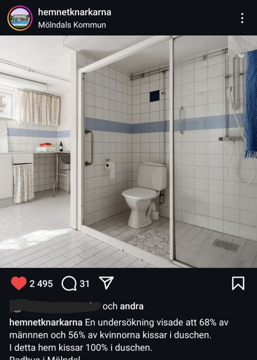 Badrum med vitt kakel, duschkabin med glasdörrar och toalett, handfat med skåp, spegel och gardin.