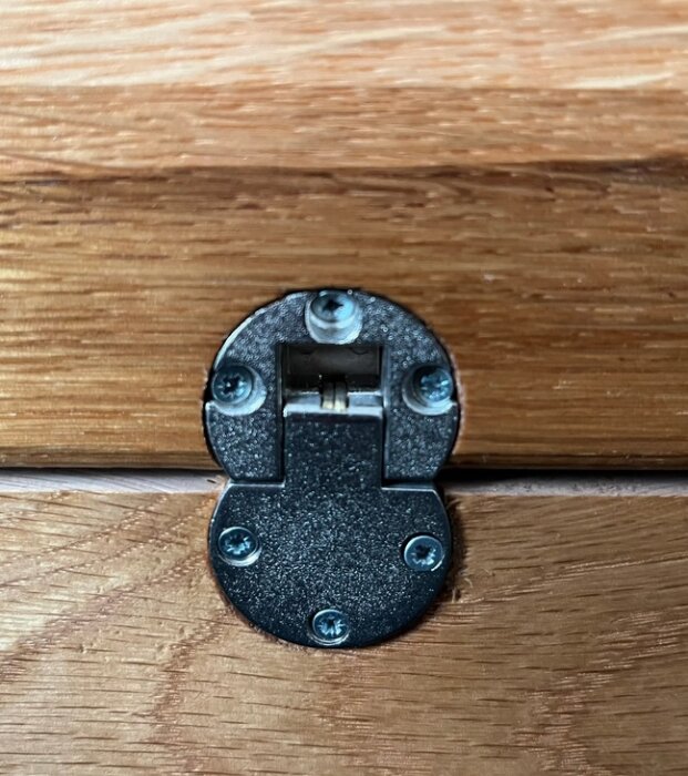 Metalliskt klaffgångjärn monterat på träyta, använt för lock till TV-hiss.