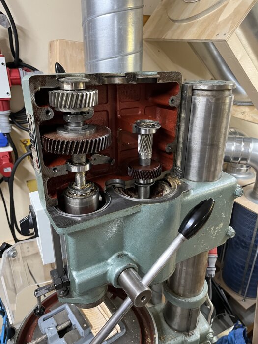 Öppen maskin med synliga kugghjul och axlar i ett verktygsrum, visar del av demonteringsprocess.