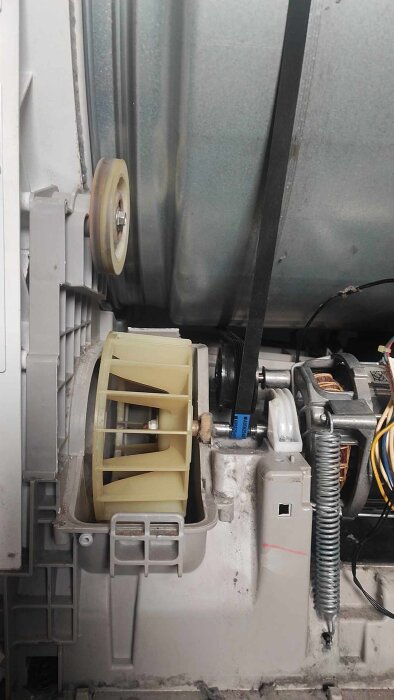 Insidan av en torktumlare med synlig rem och motor, fläkt och ledningar. En rem har bytts efter reparation av defekta komponenter.