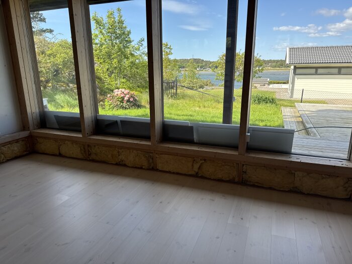 Nytt trägolv, stora fönster mot trädgård och sjö. Synlig dålig isolering vid fönstrens nederkant. Fråga om isoleringsmaterial.