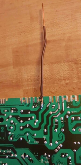 Närbild på ett kretskort med en brun tråd som är lödd på, del av en reparation.