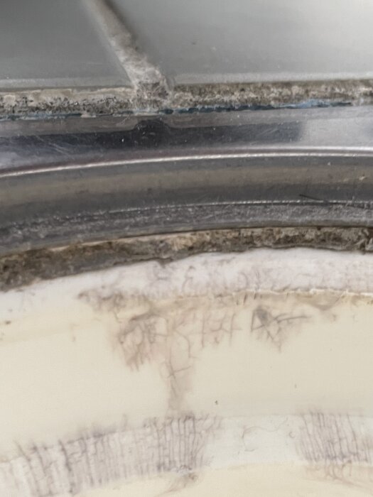 Blå plastmaterial syns under klinkers vid golvbrunnsinfästningen, vilket kan indikera potentiella problem med tätskiktet i badrumsgolvet.