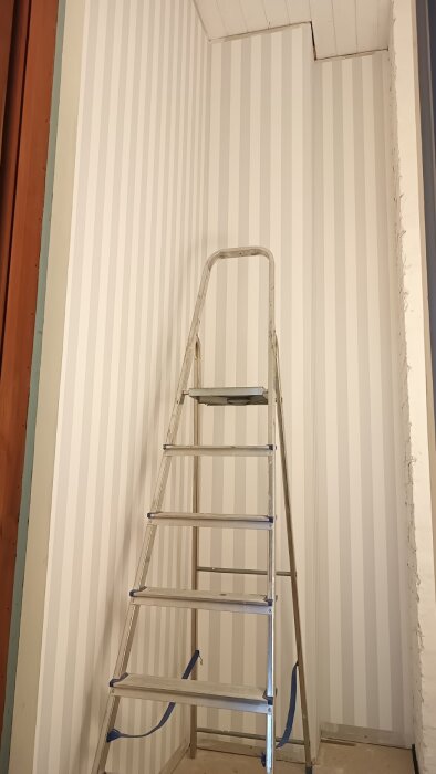 Stege mot en vägg med lodräta ränder i ett trångt utrymme med hög takhöjd.