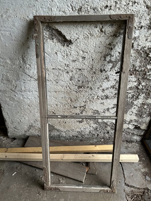 Gammal fönsterbåge lutad mot en vägg, med träplankor i bakgrunden.