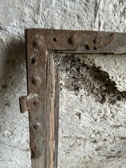 Gammal, rostig fönsterbåge med trä och metall på en vit, grov vägg.