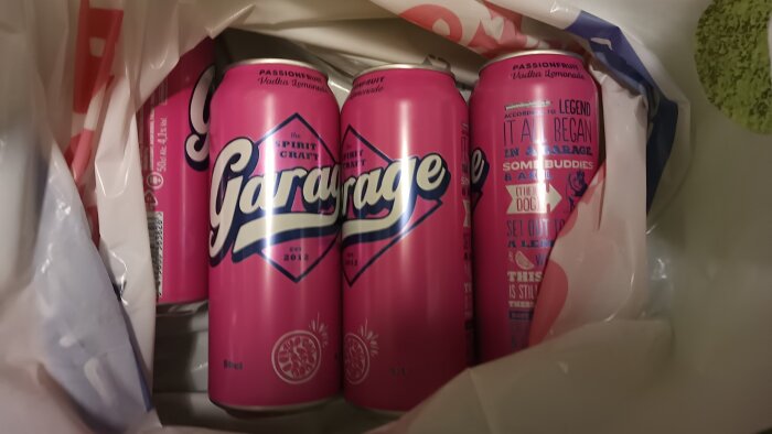 Fyra rosa burkar med drycken "Garage" med smak av passionsfrukt och vodka, delvis inslagna i en plastpåse.
