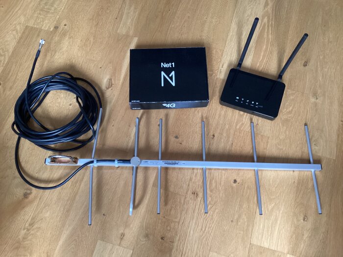 4G-router med antenner och kablar på ett trägolv, tillsammans med en Net1-förpackning.