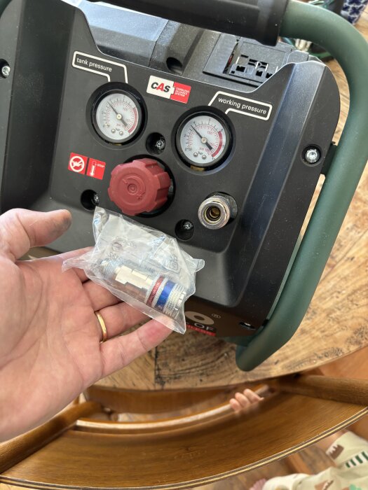 En kompressor med Cejn esafe-koppling visas, hålls av en hand över ett träbord. Två tryckmätare och en röd ventilknapp är synliga.