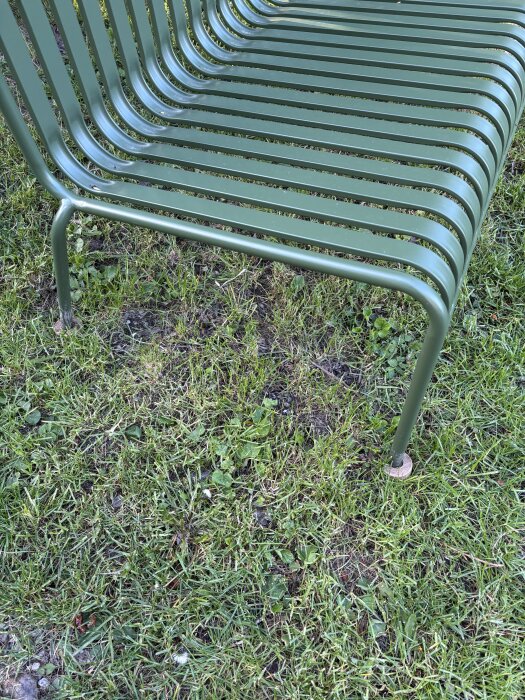 Grön metallbänk i trädgård, fotad enkligt från sidan, stående på gräs.