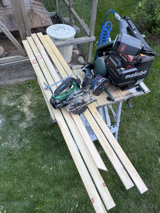 Cirkelsåg, kompressor och träplankor på ett arbetsbord vid en kaninbur.