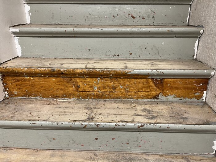 Gammal trätrappa med slitna målade sättsteg och trä som delvis blottats, tidigare täckt med korkmatta och en noslist av metall.