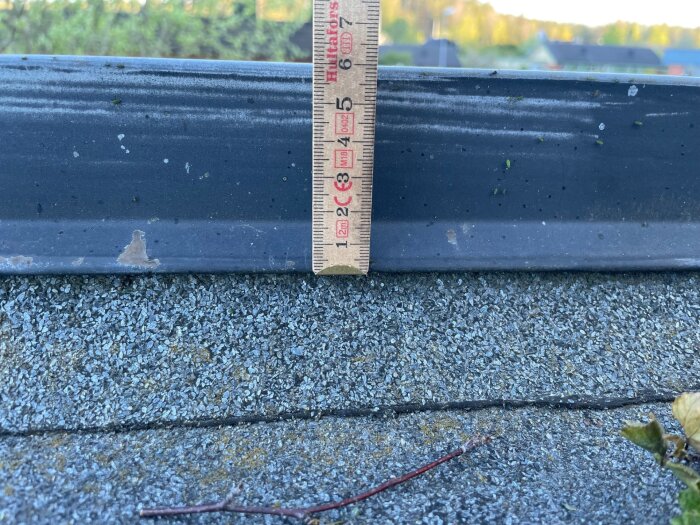 En närbild på en grå plåtprofil vid takfot, med ett måttband som visar plåtens höjd, är tagen utomhus.