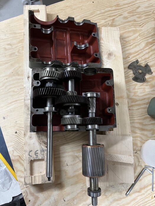 Växellåda med flera kugghjul och axlar ligger demonterad på en träbänk.