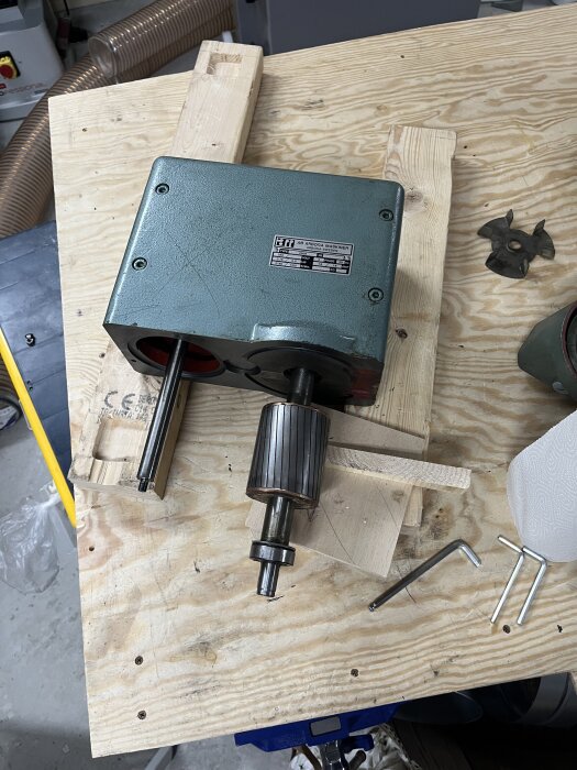 En ihopsatt maskindel med ett distansverktyg och insexnycklar liggandes på ett arbetsbord av trä.