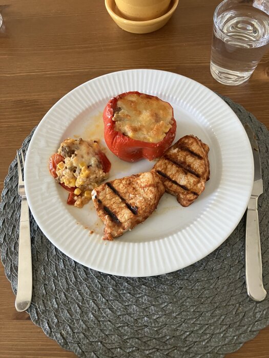 Fylld paprika med ost och grönsaker samt grillad fläskytterfilé serverad på en vit tallrik, placerad på ett bord med glas och bestick.