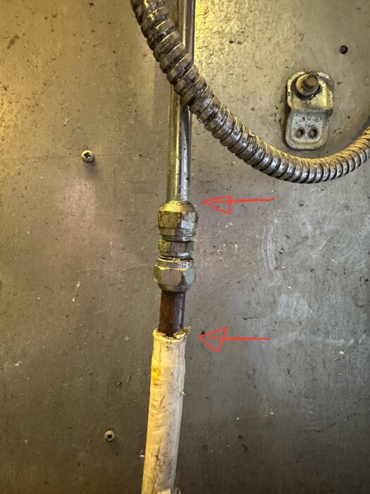 Vattenrör i garage med två läckande anslutningar markerade med röda pilar.