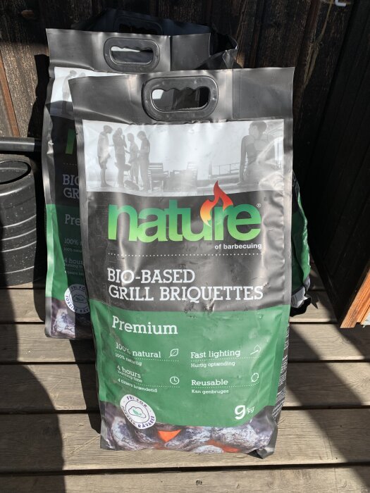 Två påsar med naturbaserade grillbriketter på en träaltan, märkta som premium och 100% naturliga.