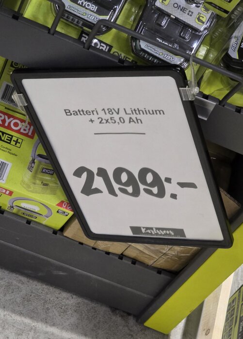 Skylt för batteripaket: "Batteri 18V Lithium + 2x5,0 Ah" för 2199 kr, omgiven av Ryobi-produkter.