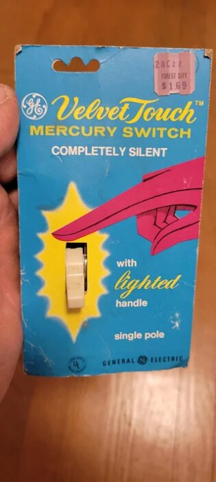 Förpackning av GE Velvet Touch kvicksilverbrytare med texten "completely silent" och "with lighted handle", hålls i en hand.