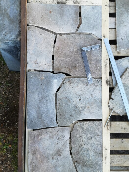 Grå naturstenar på träram med vinkelhake och linjal vid sidan, del av Schingeltakprojekt med dubbel tätning.