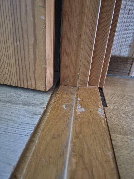 Tröskel med slitet trä och ojämn kant mellan laminatgolv och trävid dörröppning i renoveringsprojekt.