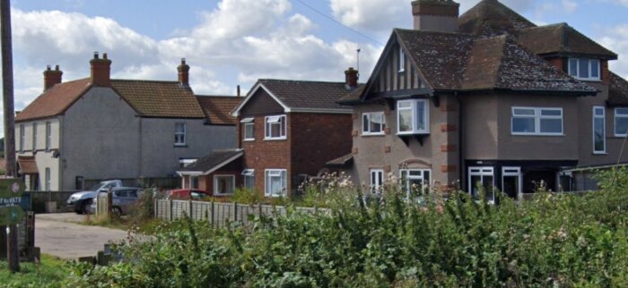 Nya hus på tidigare tomt vid gata med flera fordon parkerade längs staketet och grönska i förgrunden.