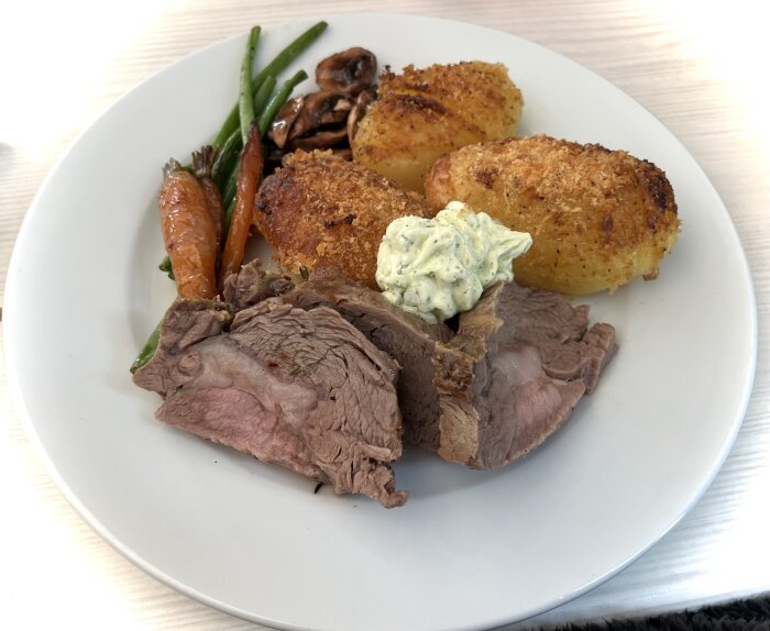 Tallrik med kalventrecote, hasselbackspotatis, vitlökssmör, ugnsvarma grönsaker, morötter och champinjoner.